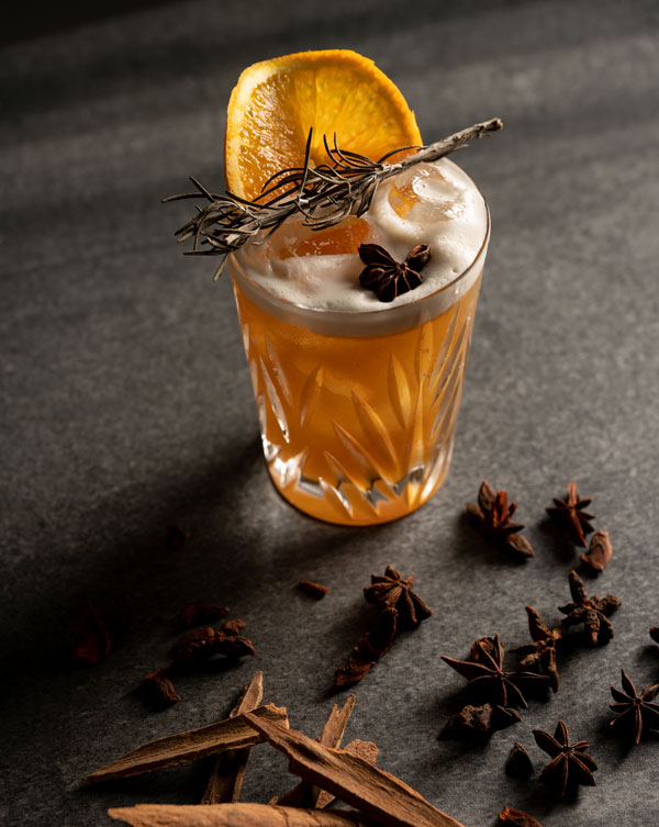 Amber color cocktail with foam with orange, clove and cinnamon
