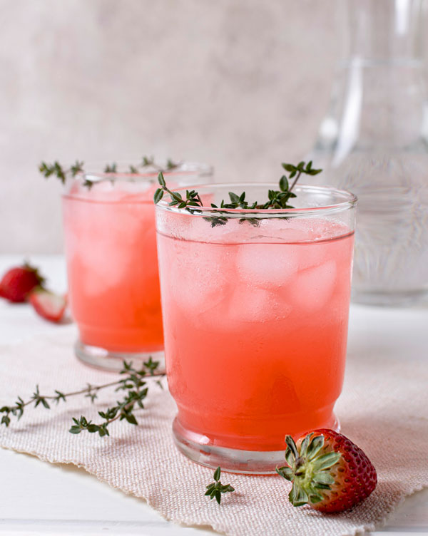 Two pink colored cocktail with strawberries around