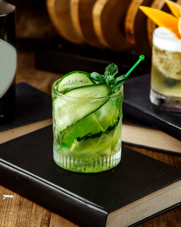 Green cocktail with cucumber slices inside on top of a black book