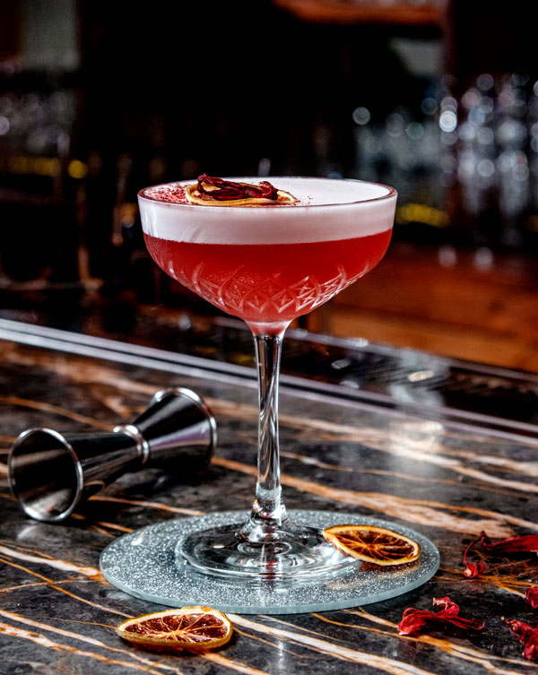 Pink cocktail with foam orange slices and jigger around the glass